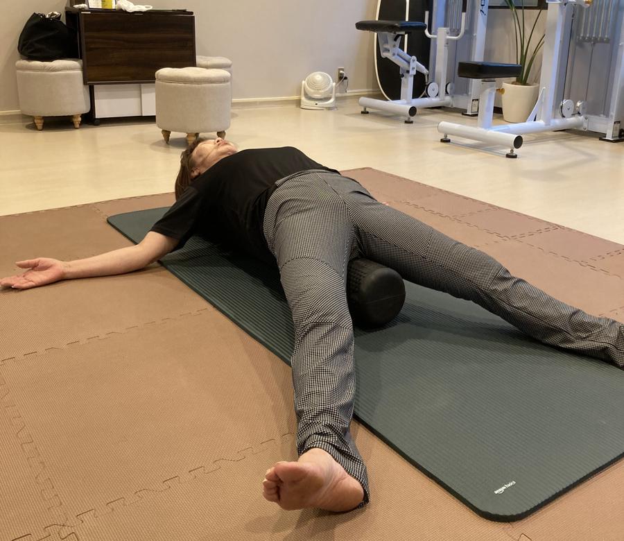 ストレッチポールの上にあお向けになり、両腕を広げて背骨まわりをゆるめるお客様