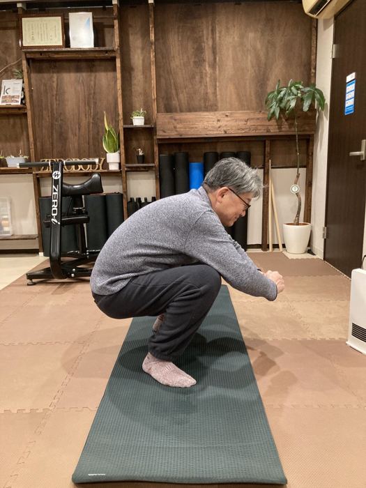 マットの上で深くしゃがむシニアの男性