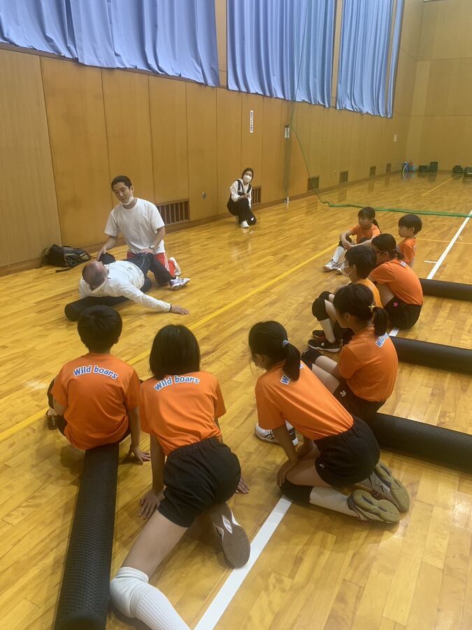 体育館で院長の説明を聞きながらポールストレッチをする子どもたち