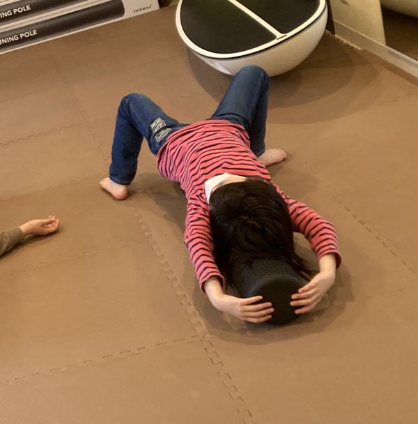 女の子がストレッチポールに頭をのせて寝転び、背中を伸ばしている様子