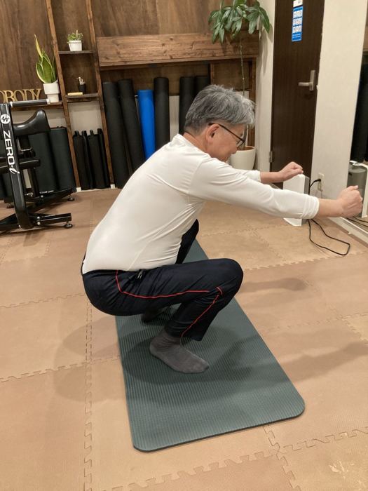 腕を前に伸ばして深くしゃがむシニアの男性