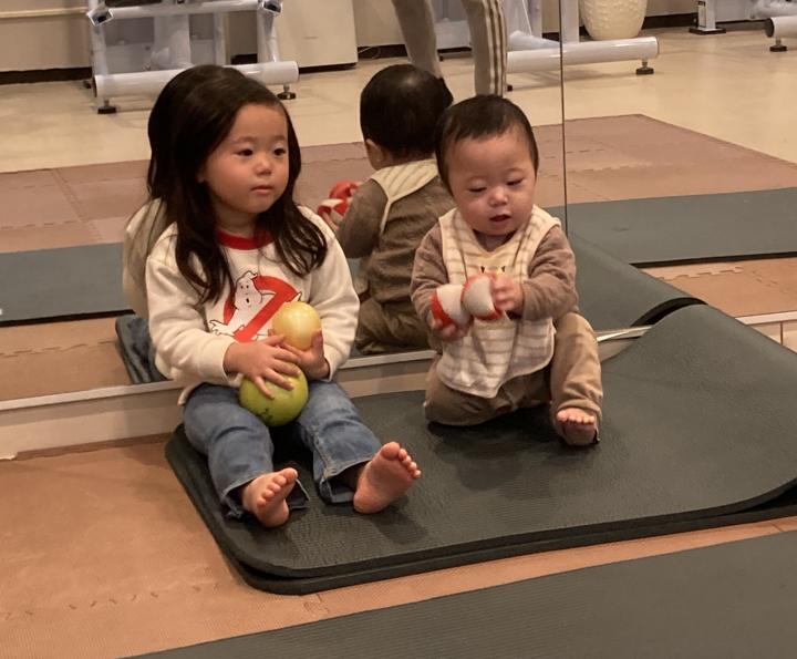 レッスン中、マットの上に座ってボールで遊ぶ小さな子どもたち