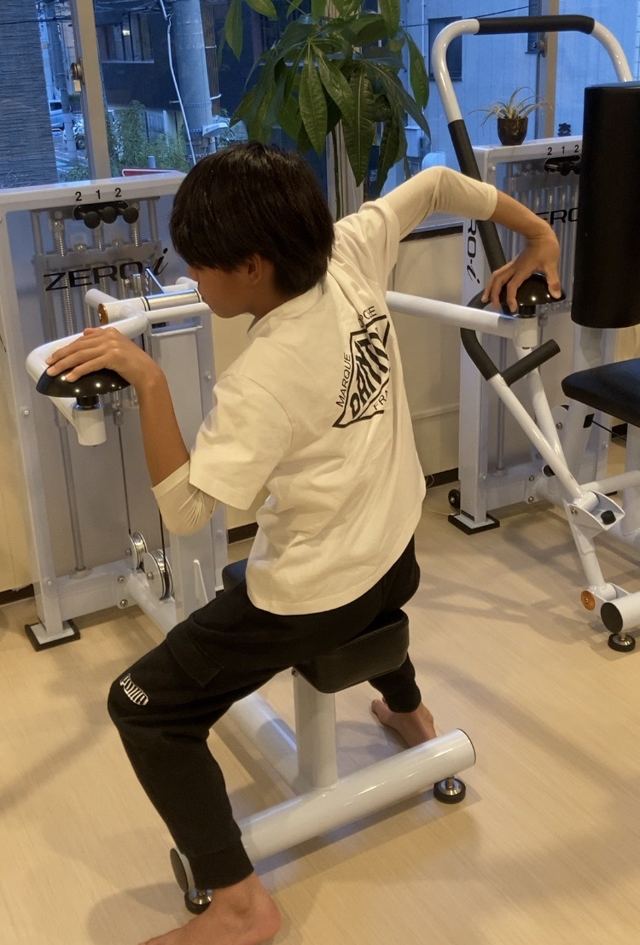 男の子がストレッチマシンに腕をかけて、肩まわりを伸ばす様子